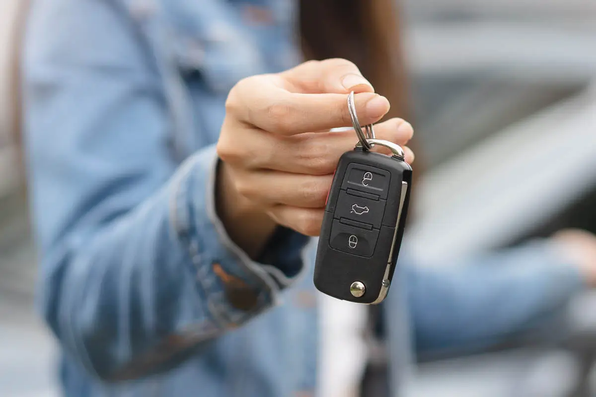 Eine Hand hält einen Autoschlüssel mit Fernbedienung in die Kamera; der Hintergrund ist unscharf, es wirkt wie eine Fahrzeugübergabe.